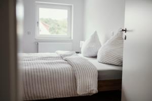 a white bed with striped sheets and a window at Ferienwohnung Schwalbenflug in Naumburg