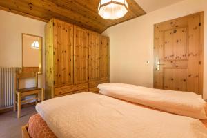 two beds in a bedroom with wooden cabinets and a chair at Casa Lorenz 4 in Canazei