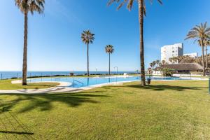 a swimming pool with palm trees and the ocean at Mi capricho Beachfront Apt in Mijas