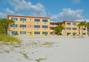 a large yellow building with palm trees in front of a beach at Page Terrace Beachfront Hotel in St. Pete Beach