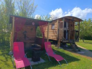 a small cabin with two pink chairs in front of it at Roulotte Ô Rêves Atypiques in Boucé