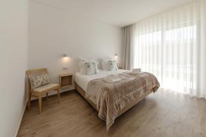 a white bedroom with a bed and a chair at Terra - B&P Infinity House in São Martinho do Porto
