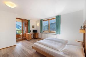 a bedroom with a bed and a desk and windows at Al Cargá San Vigilio di Marebbe in San Vigilio Di Marebbe