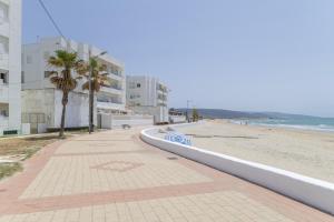 a sidewalk next to a beach with palm trees and buildings at Apartamento a pie de playa in Barbate