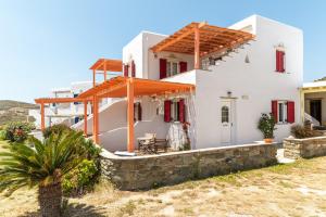 a white house with red windows and a stone wall at Anemologio 201 Tinos in Agios Ioannis