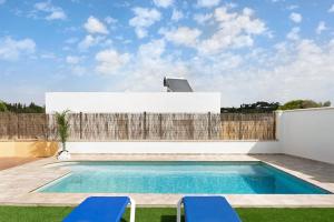 a swimming pool with two blue chairs and a fence at Villa Montemedio - Paco in El Soto