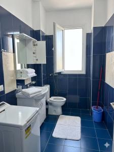a blue tiled bathroom with a toilet and a window at Radhima Beach Apartments in Vlorë