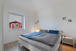 a white bedroom with a bed and a window at Seelenwärmerstuuv in Kronprinzenkoog