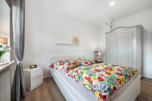 a white bedroom with a bed with a colorful comforter at Ferienhaus Auszeit Meer in Cuxhaven