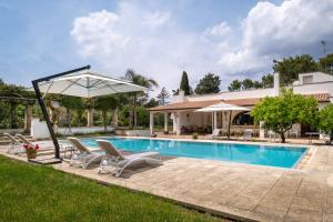 a swimming pool with chairs and an umbrella next to a house at Tenuta Il Carretto in Monteroni di Lecce