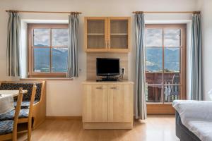 a living room with a tv and two windows at Woehrmannhof Apt Spinnrad in Feldthurns
