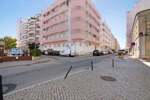 a street with a pink building and cars parked on the street at Âncora B in Monte Gordo