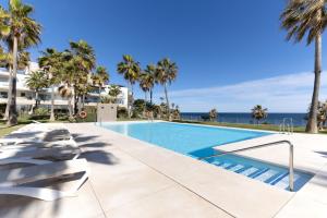 a swimming pool with palm trees and the ocean at Modern frontline beach - Estepona in Estepona