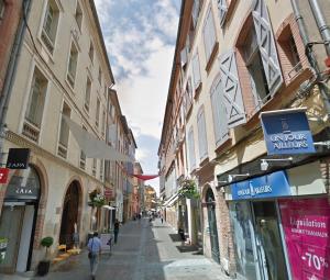 a street with buildings and a man walking down the street at Le beau 25 République in Montauban