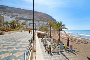 a beach with chairs and umbrellas and the ocean at Paraiso Playa Taurito in Taurito