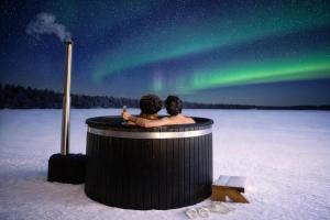 a couple sitting in a hot tub looking at the northern lights at Sonka Resort Mirror House with Lake View in Rovaniemi +17 photos