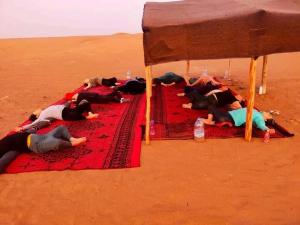 a group of people laying on a red rug in the desert at Dunes Activity Camp in Mhamid