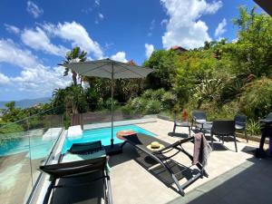 a patio with chairs and an umbrella next to a swimming pool at Villa APOLLINAIRE in Les Trois-Îlets