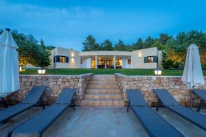 a house with a stone wall and chairs and umbrellas at Sa Lluna in Sant Josep