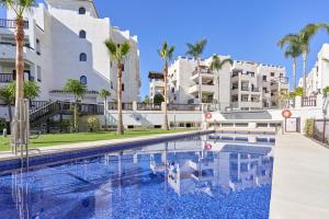 a swimming pool in front of a building with palm trees at El ático del Oasis in Salobreña