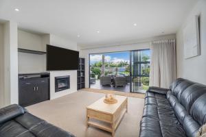 a living room with a black leather couch and a tv at Villa One on the Waterways - Pool, Spa Pool, Tennis in Whitianga