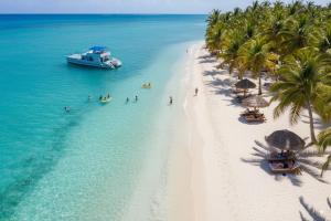 a boat in the water next to a beach with palm trees at beautiful vacation Sol Caribe in Punta Cana