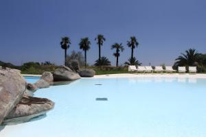 a large swimming pool with rocks and palm trees at Li Conchi 44 in Castiadas