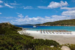 a beach with chairs and umbrellas and a boat in the water at Trilocale Fiordaliso in Stintino