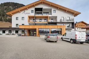 ein Gebäude mit zwei auf einem Parkplatz geparkten Autos in der Unterkunft Hotel Murrer relaxe.nature.gusto in Sarntal