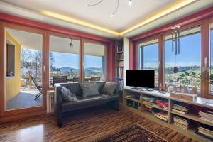 a living room with a couch and a tv and windows at Lichtblick in Weiler-Simmerberg