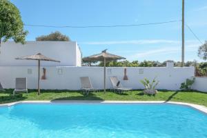 a pool with chairs and umbrellas next to a white wall at Casa Nesenka 1 in Zahora