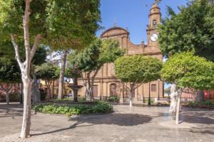 a building with a clock tower and a building with trees at Ático San Miguel vacacional in Gáldar