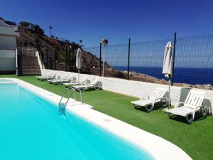 a pool with chairs and umbrellas next to the ocean at Balcón de Amadores - Beach view in Puerto Rico de Gran Canaria