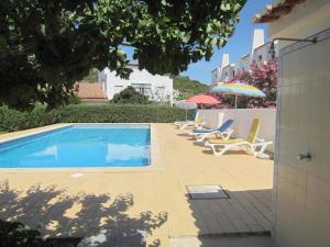 a swimming pool with chairs and umbrellas next to a building at Casa Fernandes in Burgau