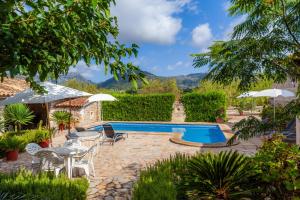 a pool in a garden with tables and chairs and umbrellas at S'alqueria Vell in Campanet