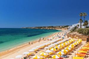 a beach with yellow and white umbrellas and the ocean at Casa Enxame in Armação de Pêra