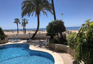 a swimming pool next to a beach with palm trees at Front Line on the beach in Calpe