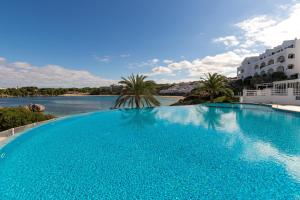 a large blue swimming pool next to a body of water at White Sands Maluz in Arenal d'en Castell