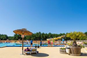 a pool at a resort with people sitting in chairs and an umbrella at Camping Les Oyats in Seignosse