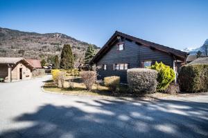 a black house with bushes in front of a driveway at Chalet 6p Classique - Les Biches in Verchaix
