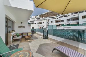 a balcony with chairs and an umbrella on a building at Eucalipto-Sun guaranteed-pool wifi in Puerto Rico de Gran Canaria