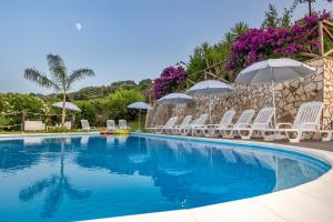 a swimming pool with white chairs and umbrellas at Arcaloro Resort Rooms in SantʼAngelo di Brolo