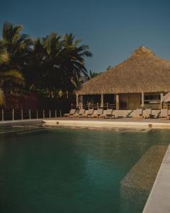 a resort with a pool with chairs and a thatch roof at Hotel Calma Celesti in Perihuete