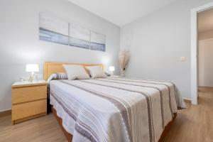 a white bedroom with a large bed and a dresser at Apartamentos Cunidor - Cunit in Cunit