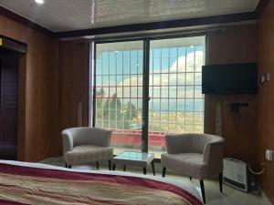 a bedroom with a bed and two chairs and a large window at Shagufta Hotel Murree in Murree