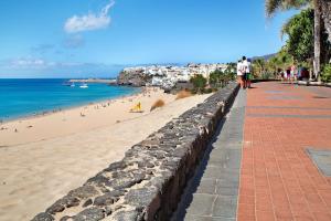 a man walking down a sidewalk next to a beach at Apartamento Playa Morro Jable 1a in Morro del Jable