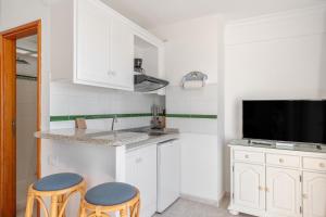 a kitchen with white cabinets and two stools and a tv at Playa Delphin 304 in Puerto Naos