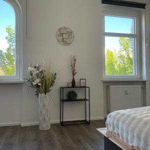 a white bedroom with a vase of flowers and two windows at Harzträume Thale in Thale