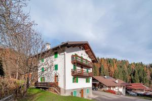 a white building with green windows on a hill at Appartamento Zopel in Falcade
