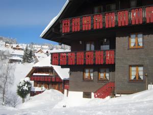 a building covered in snow with red doors and windows at Erlenhof in Todtnau